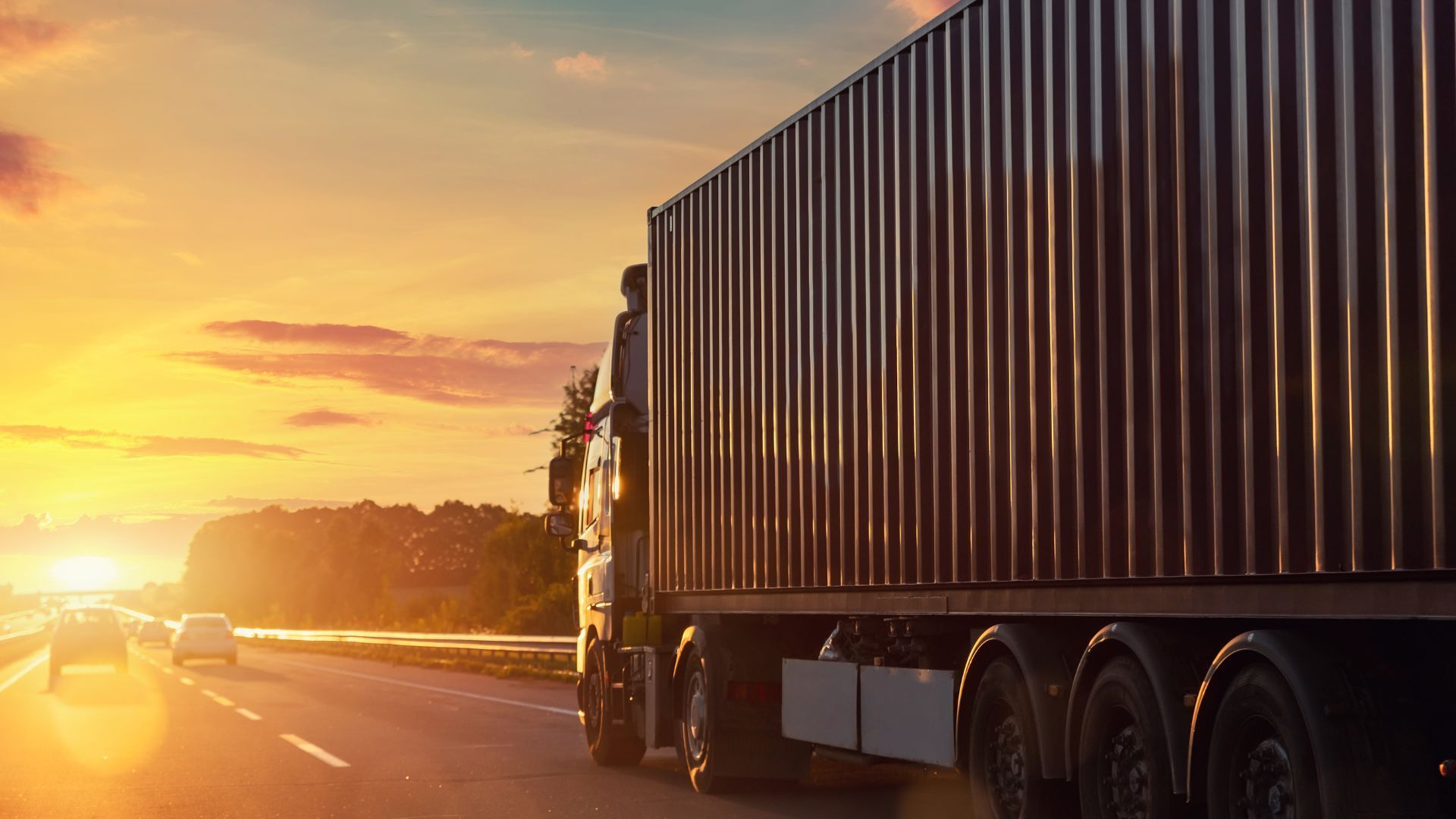 A semi truck is driving down a highway at sunset.