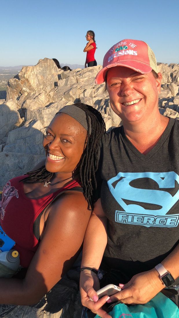 Two women are posing for a picture on top of a rocky hill . one of the women is wearing a superman shirt.