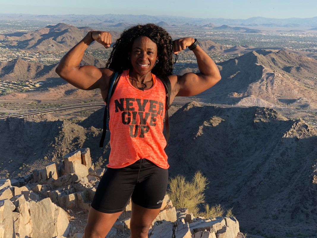 A woman is standing on top of a mountain wearing an orange tank top that says never give up.