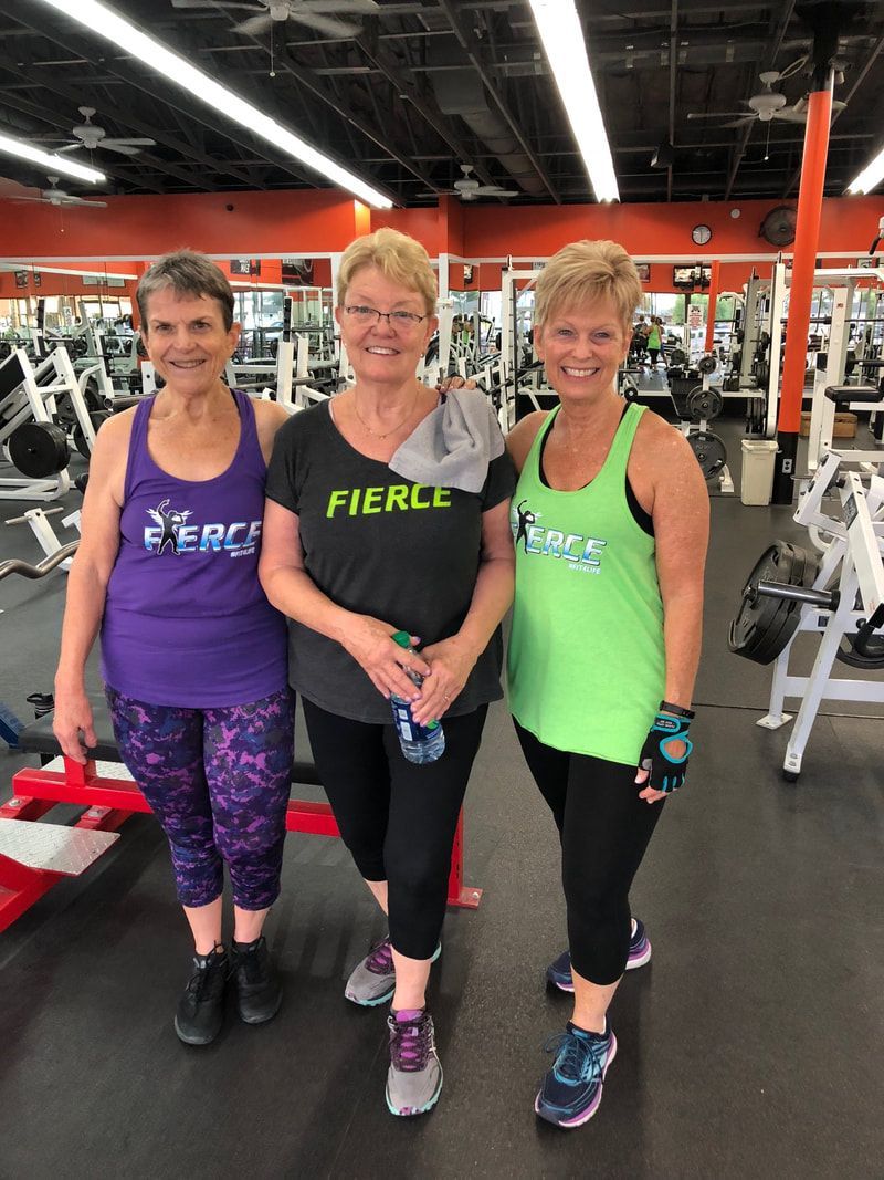 Three women are posing for a picture in a gym.