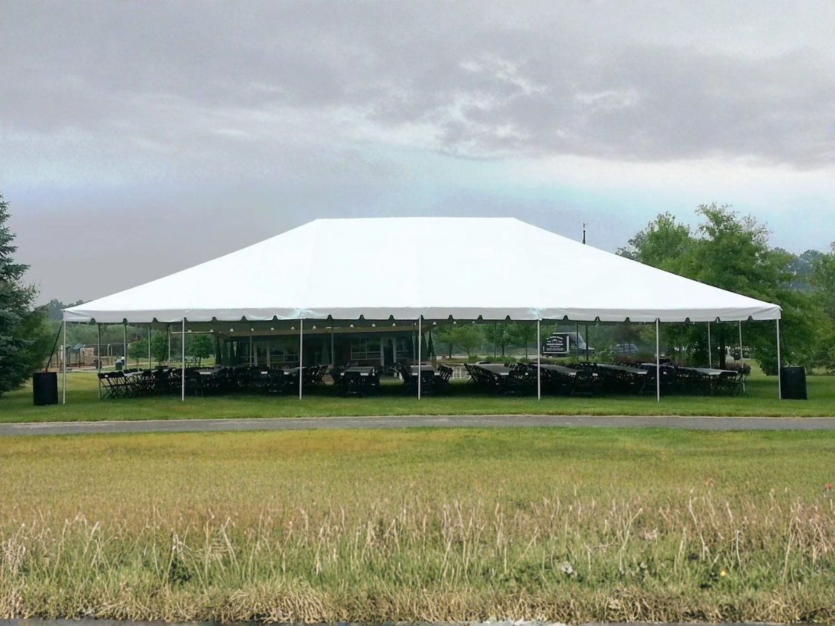 Large white event tent on a grassy field under a cloudy sky, with trees in the background.