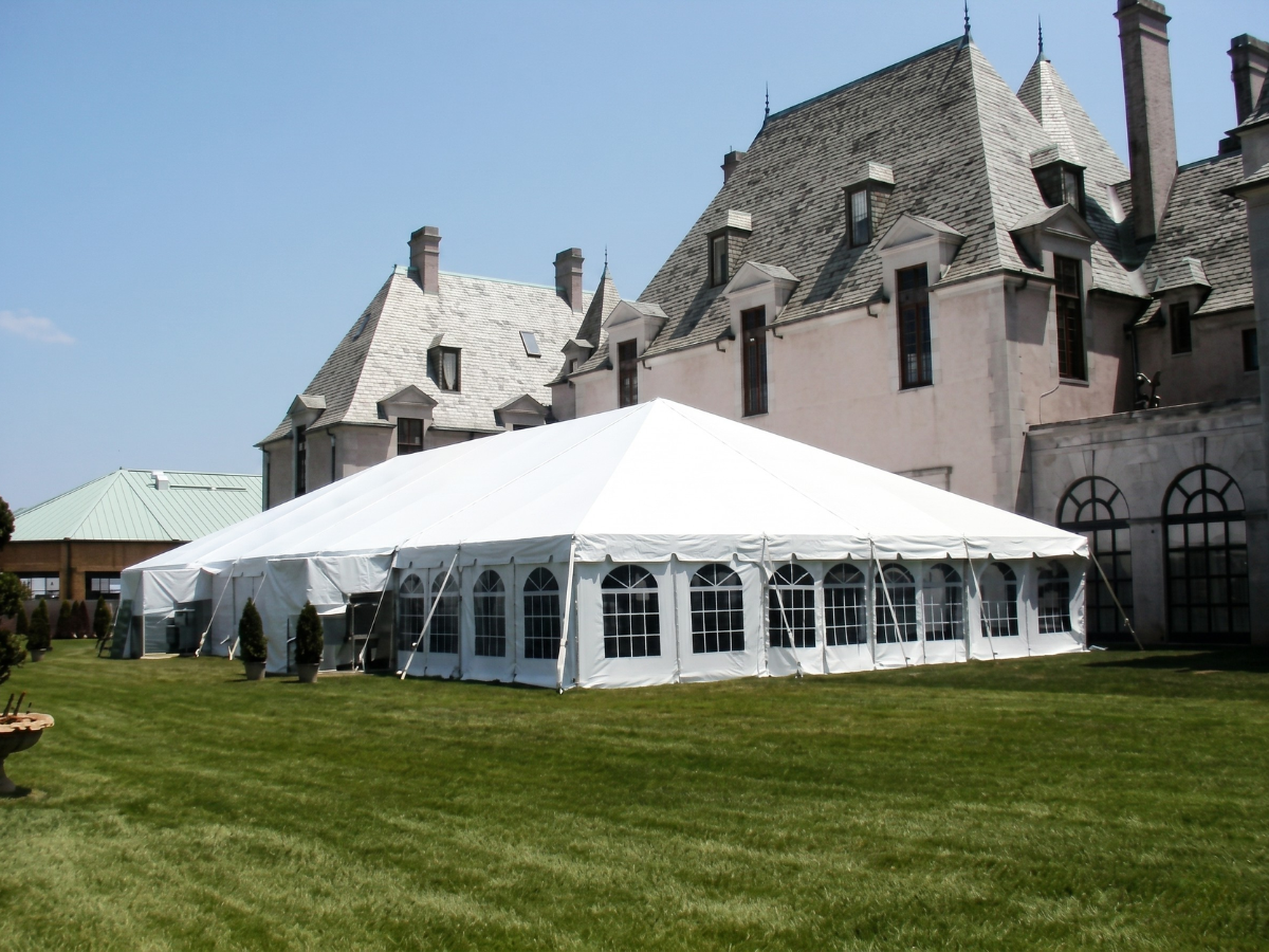Large white event tent on a lawn beside a stone castle-like building under a blue sky