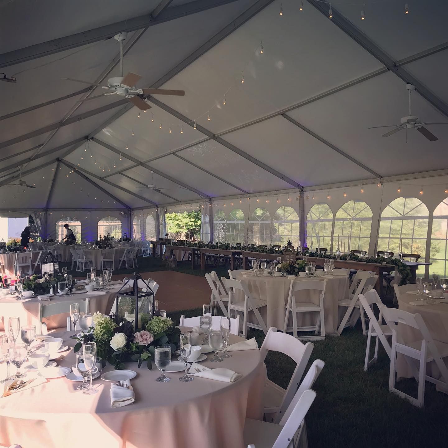 Wedding reception tent with round tables, white chairs, and floral centerpieces.