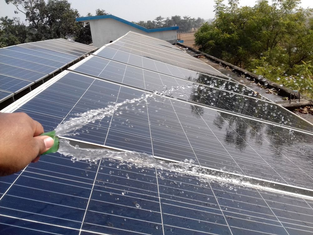 A Person is Cleaning a Solar Panel With a Green Brush — Leonard Gray Roof Tiling In Casino, NSW