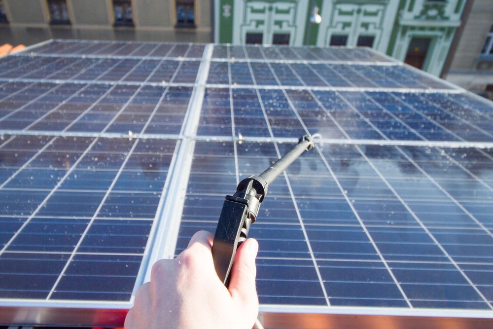 A Person is Cleaning a Solar Panel With a Spray Bottle — Leonard Gray Roof Tiling In Ballina, NSW