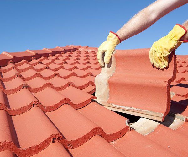 A Person Wearing Yellow Gloves is Working on a Roof — Leonard Gray Roof Tiling In Goonellabah, NSW