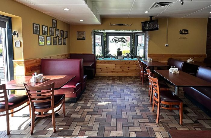 Empty restaurant dining room with booths, wooden tables, and patterned tile floor lit by daylight