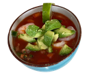 Bowl of red soup topped with avocado chunks and a green pepper strip