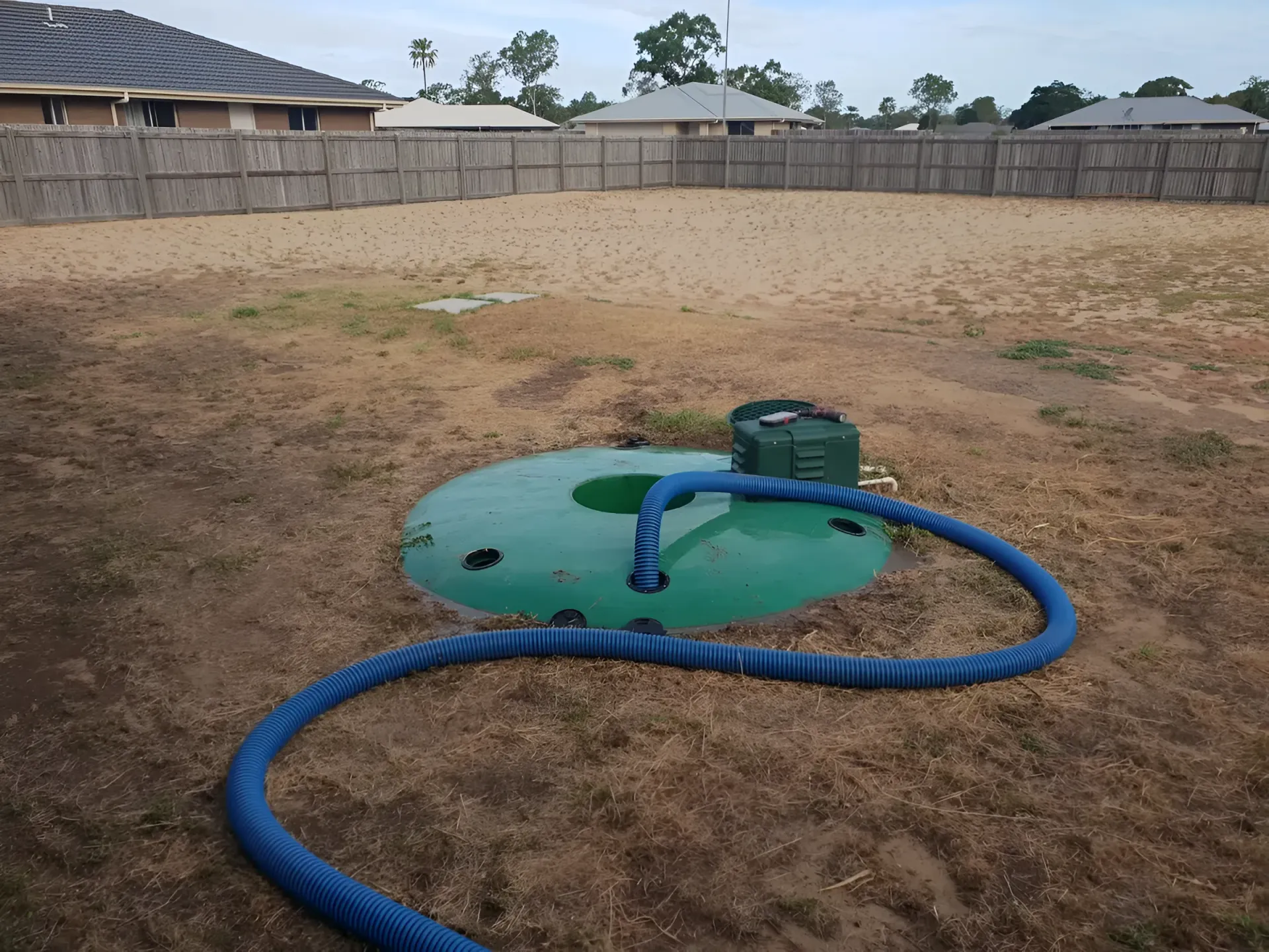 Green Septic Tank With Blue Hose in a Dry, Grassy Backyard — Paap's Cleansing Services in Branyan, QLD