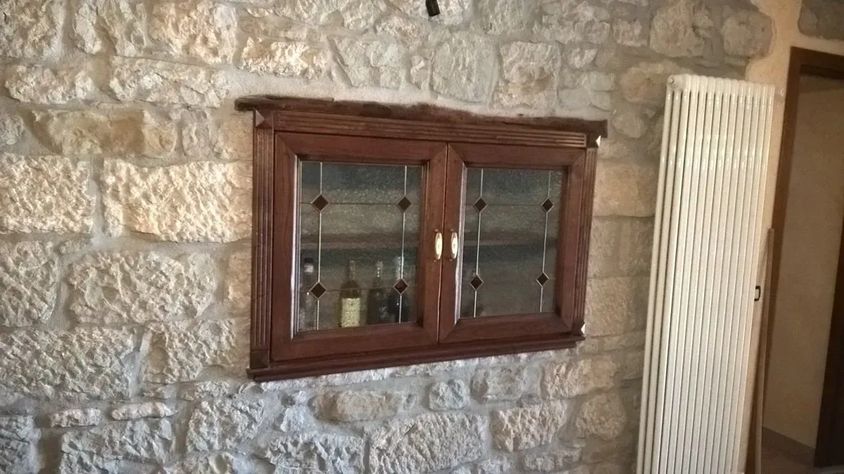 Una finestra di legno con una porta di vetro è appesa a un muro di pietra.