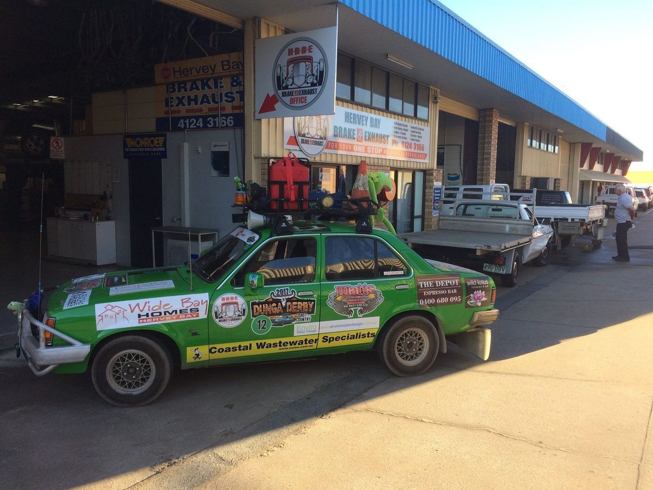 A Green Car Covered in Stickers Parked Outside a Mechanic Shop — Hervey Bay Brake and Exhaust in Pialba, QLD