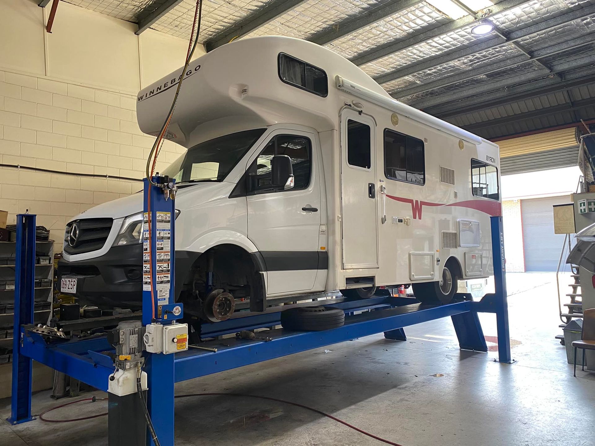 A White Rv Lifted on A Blue Four-Post Car Lift Inside a Garage — Hervey Bay Brake and Exhaust in Pialba, QLD
