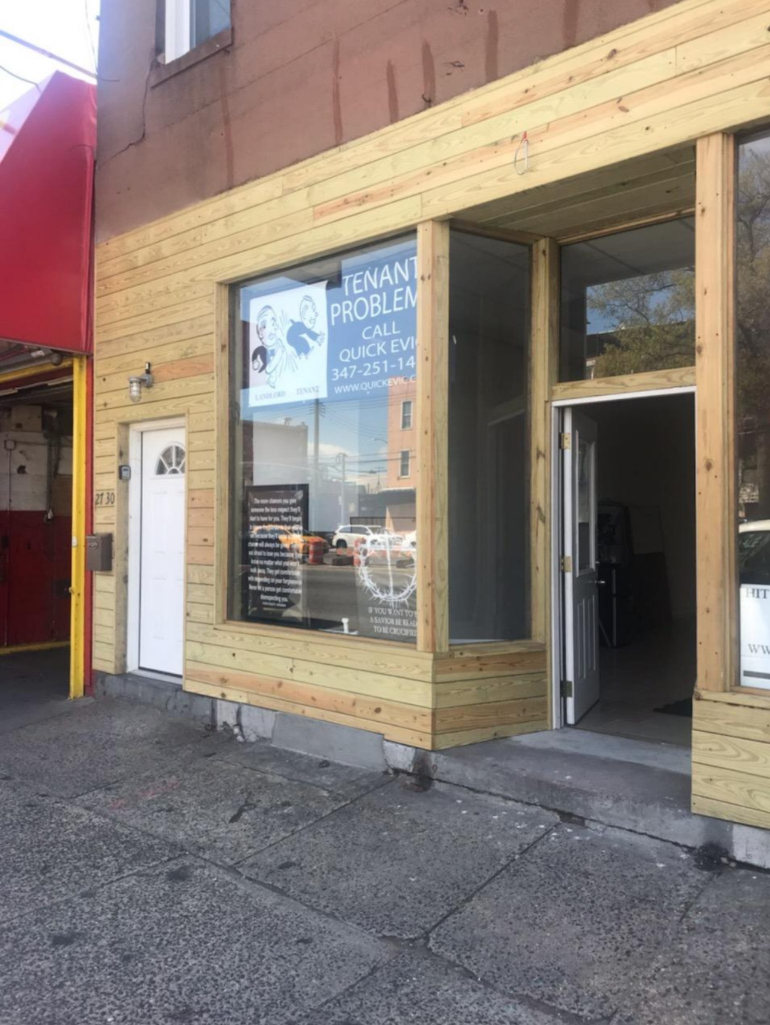 A storefront with light wood siding and a white door, featuring signage on the window about legal tenant services.