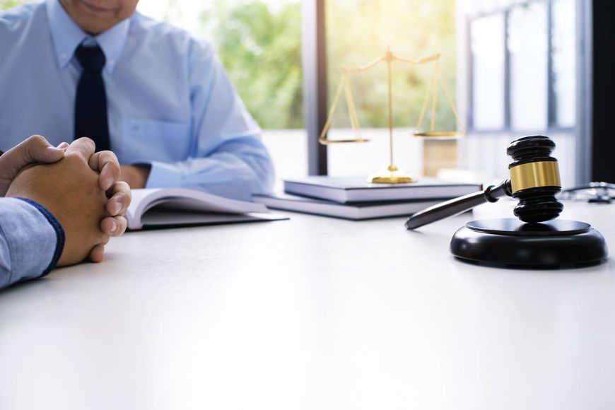 A person sits at a desk with a gavel and a scale of justice, suggesting a legal or judicial consultation.