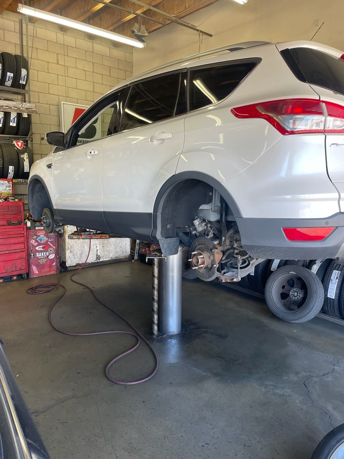 A white SUV raised on a hydraulic lift inside a repair shop, with one wheel removed.