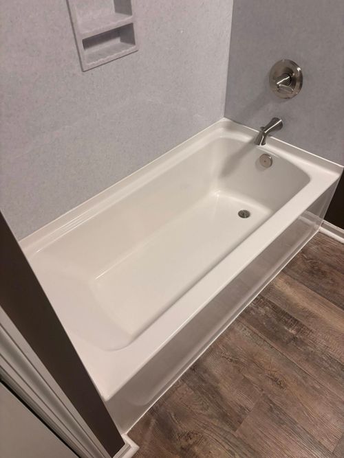 White bathtub with chrome faucet in a bathroom with wood-look flooring.