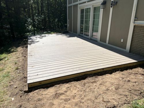 Wooden deck patio beside a house, with sliding glass doors and trees in the background.