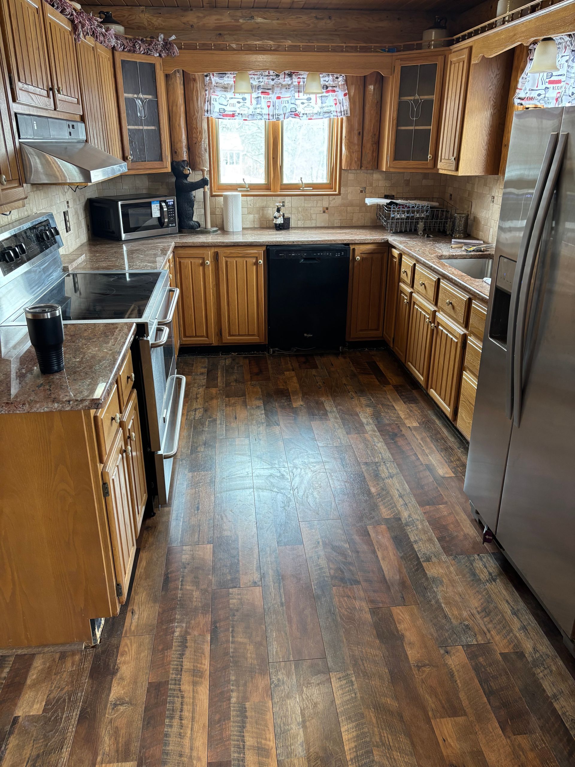 Wood-paneled kitchen with wood cabinets, stainless fridge, and window over the sink