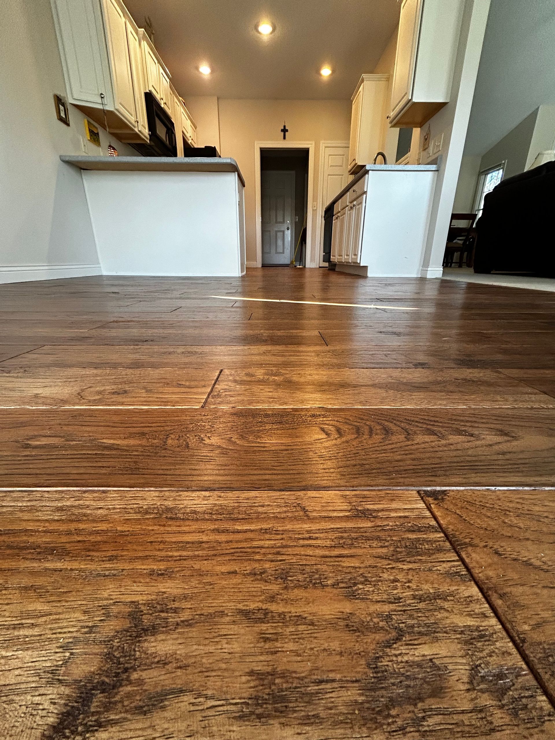 Low-angle view of a rustic wood floor leading to a bright hallway with white walls and a doorway.