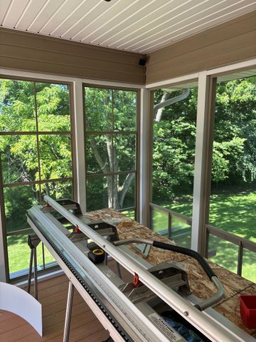 Covered porch with aluminum tracks, tools, and a workbench facing a green backyard through screened windows