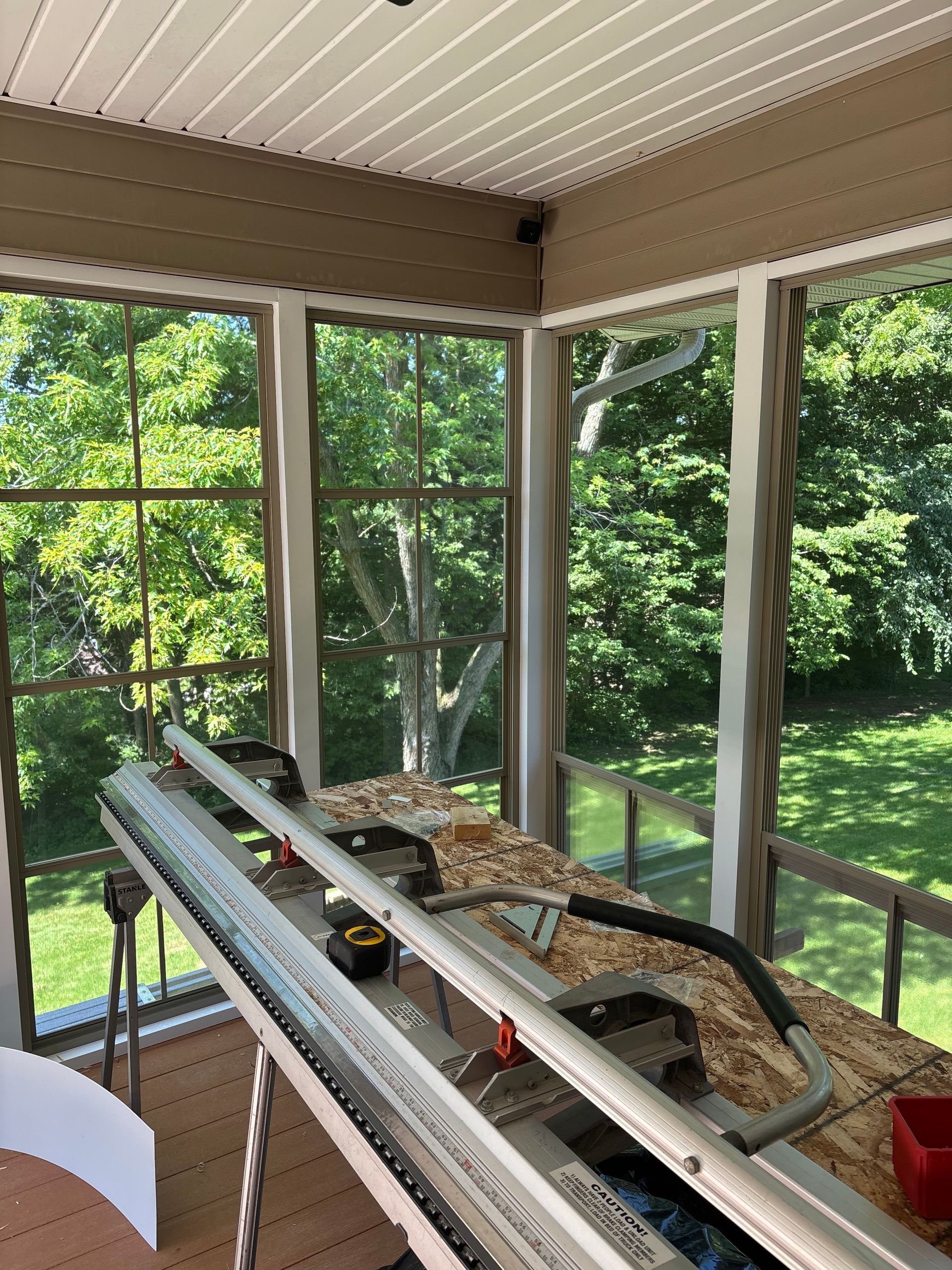 Screened porch with ladder, tools, and materials on railing overlooking a green backyard
