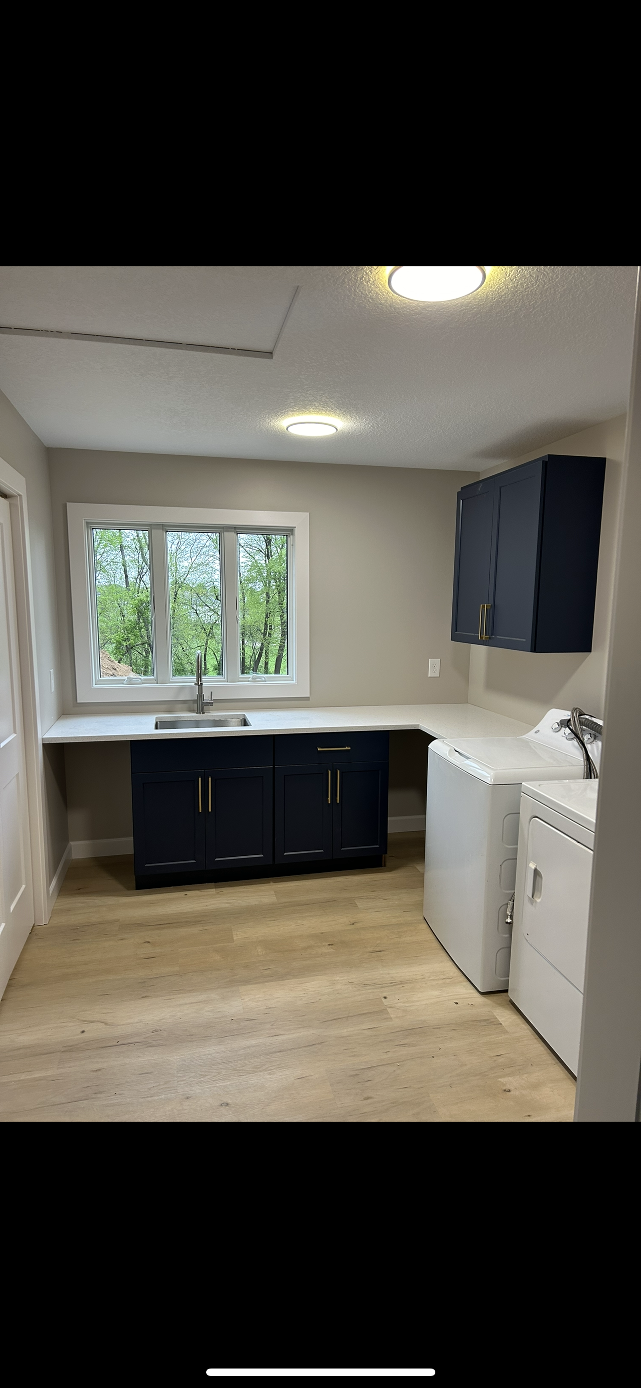 Small kitchen or laundry room with dark cabinets, white appliances, window, and light wood floor.