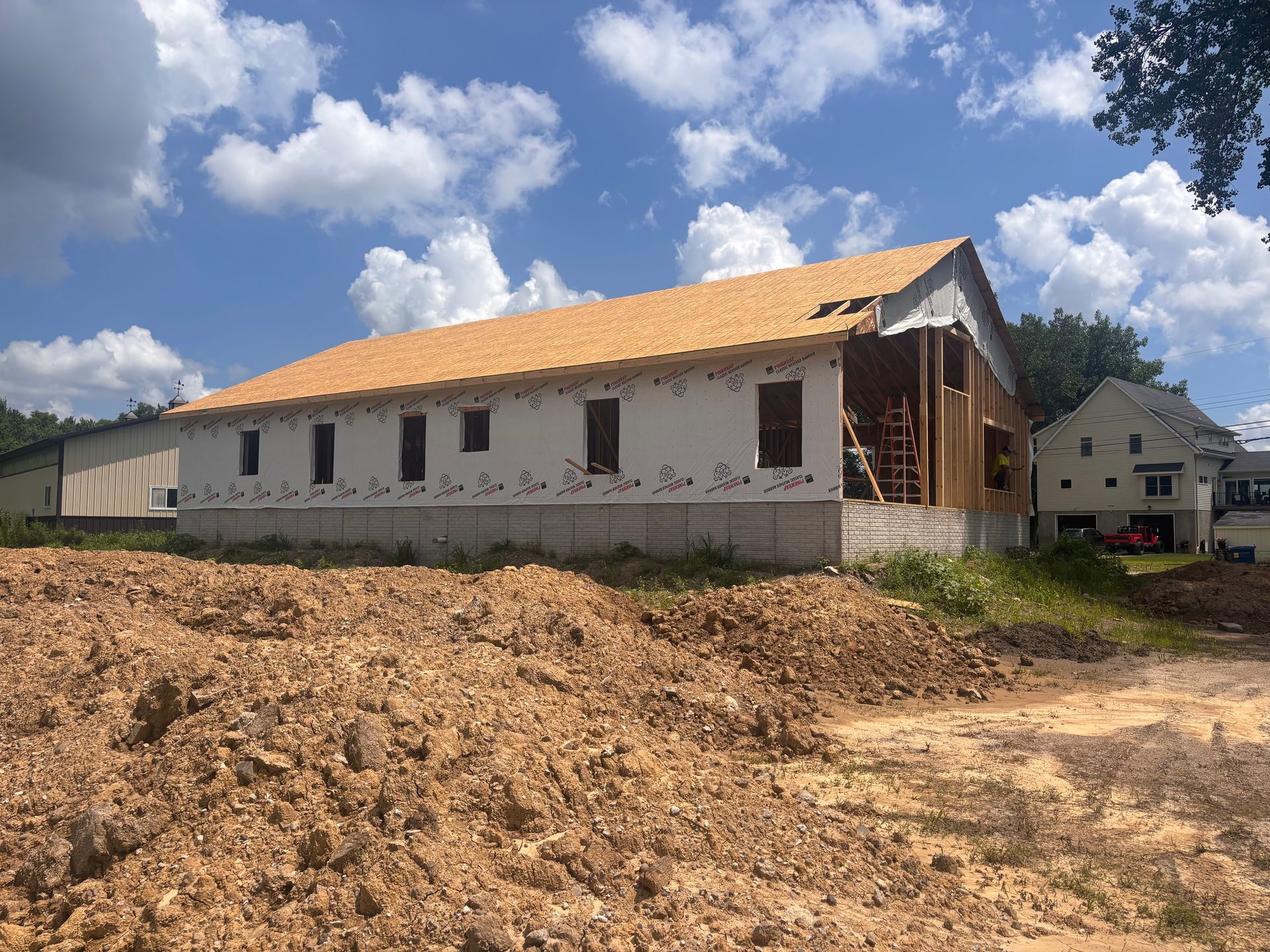 Partially built white house with orange roof on a dirt lot under a cloudy blue sky