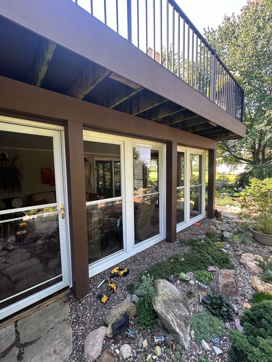 House exterior with large windows, balcony railing, and rocky landscaping in sunlight