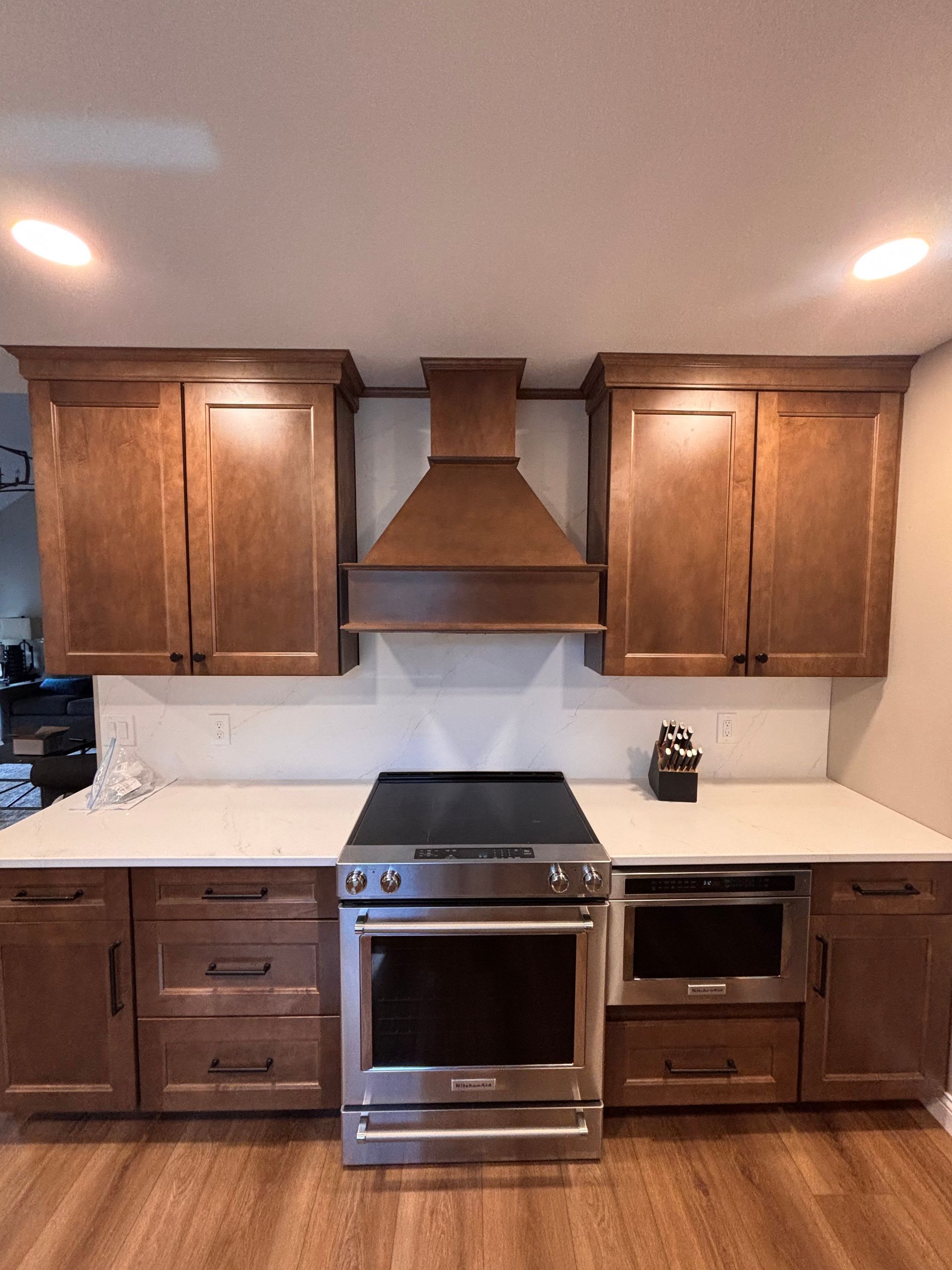 Kitchen with wooden cabinets, stainless steel stove, and range hood on a white backsplash.