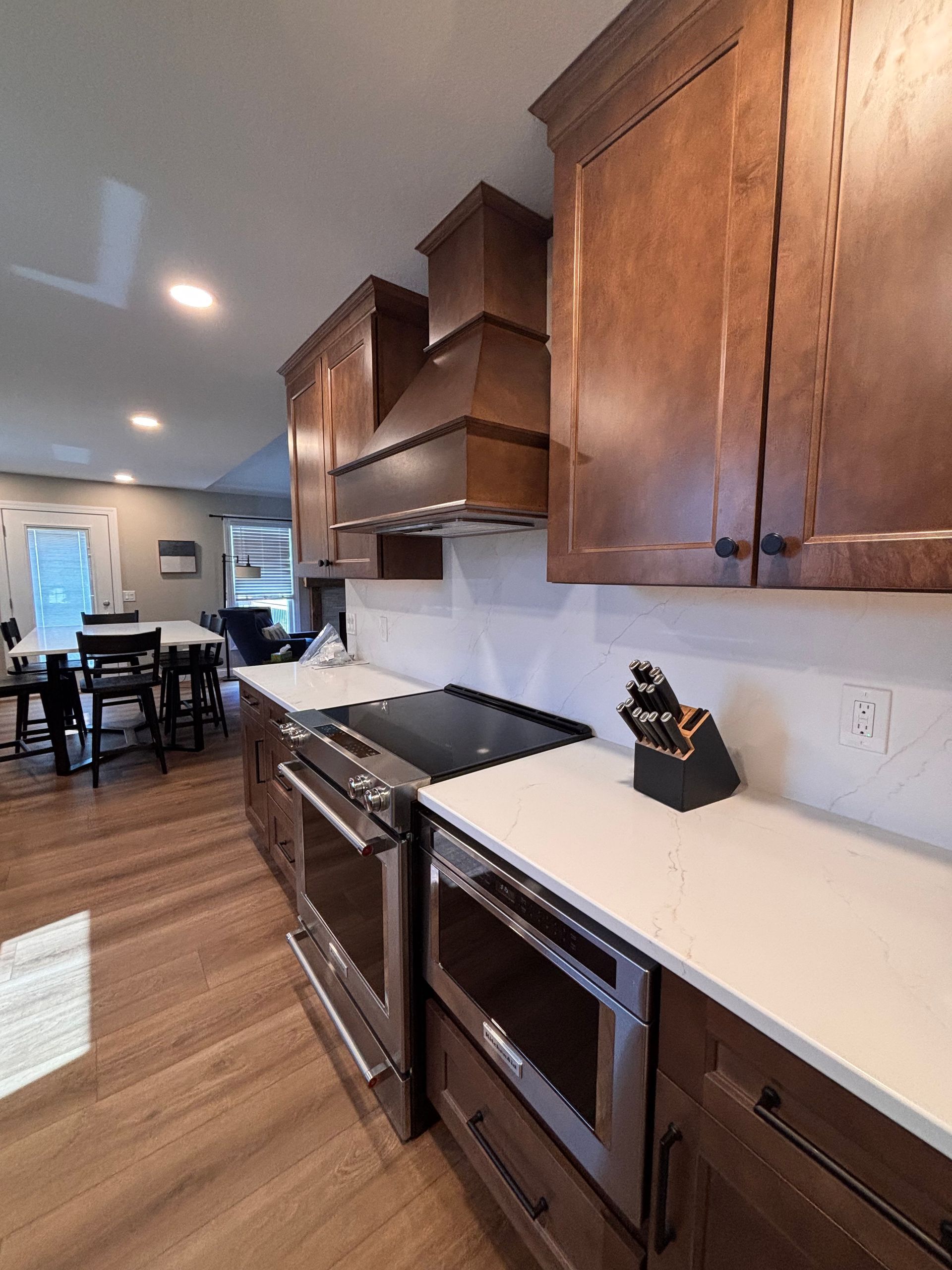 Modern kitchen with wood cabinets, white counters, stainless oven, and open view to dining area