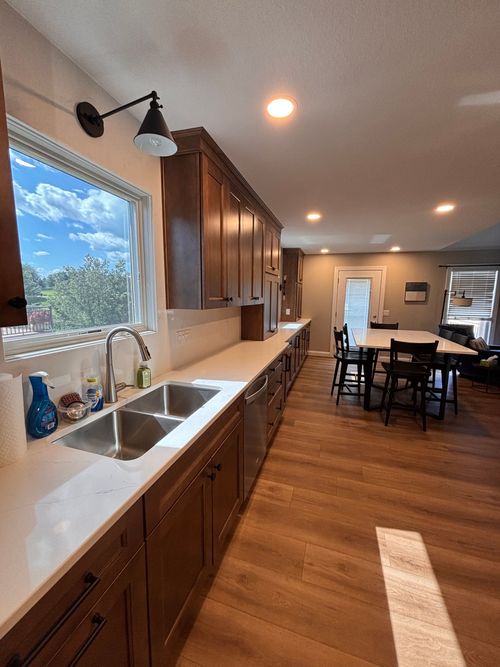 Bright kitchen with wood cabinets, white countertops, large window, and dining table in the background