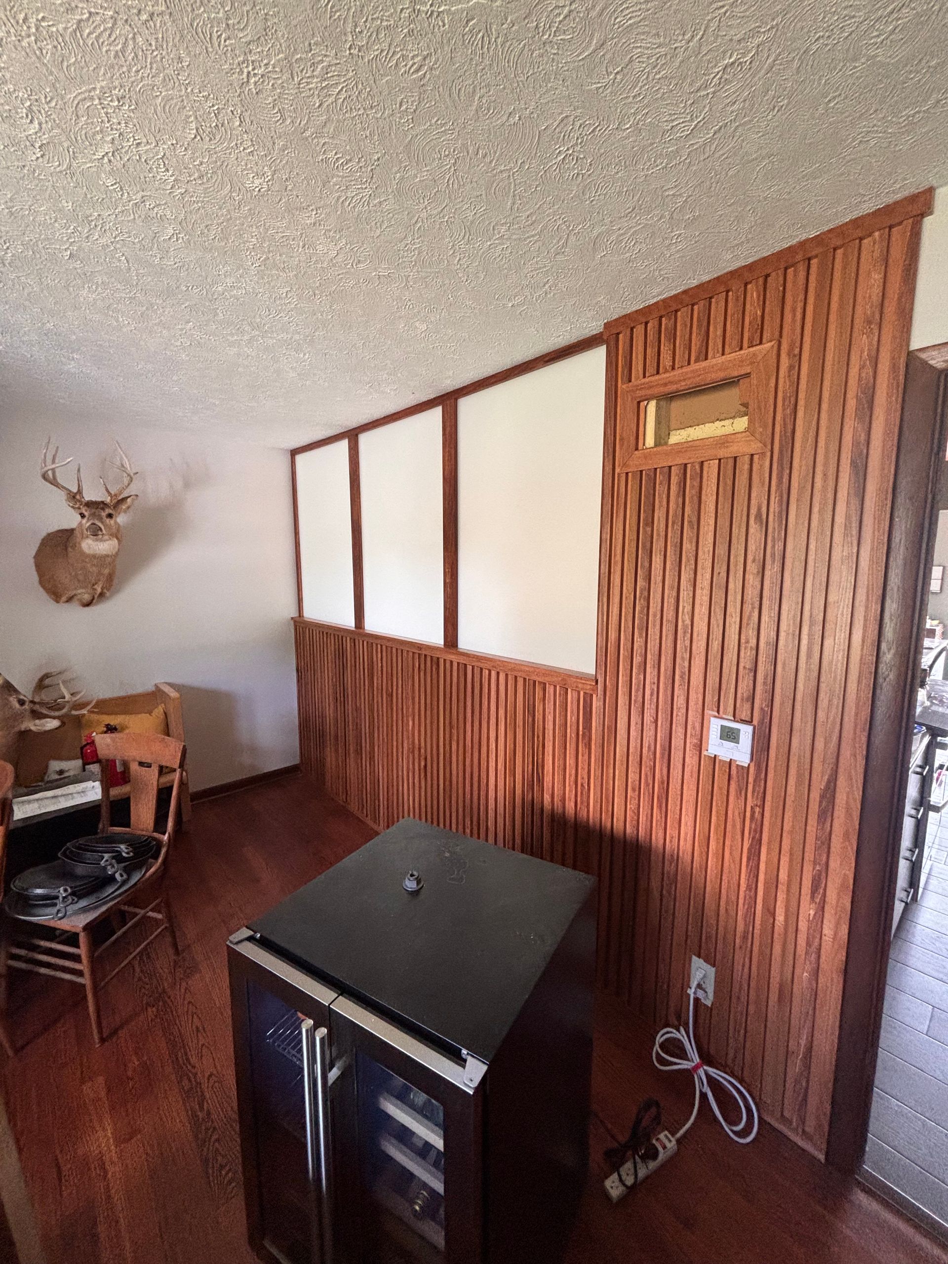 Wood-paneled room with a black mini fridge, white wall panels, and mounted deer head decor