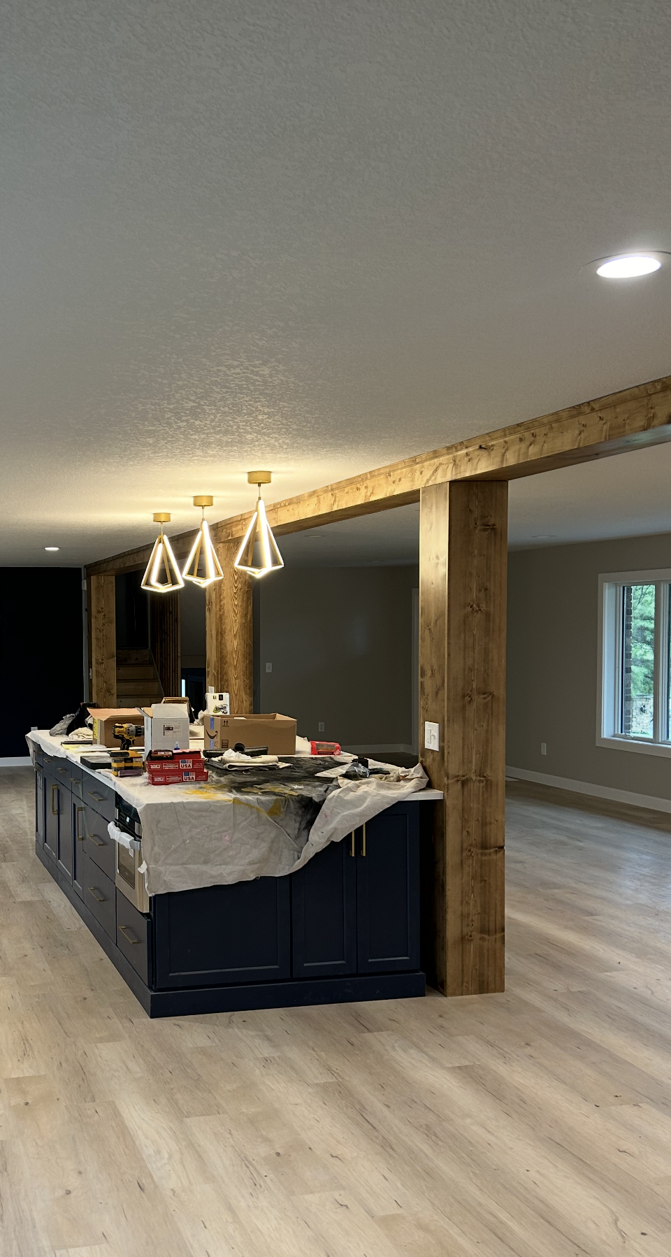 Unfinished basement kitchen with island, exposed wood beam, pendant lights, and light wood flooring.