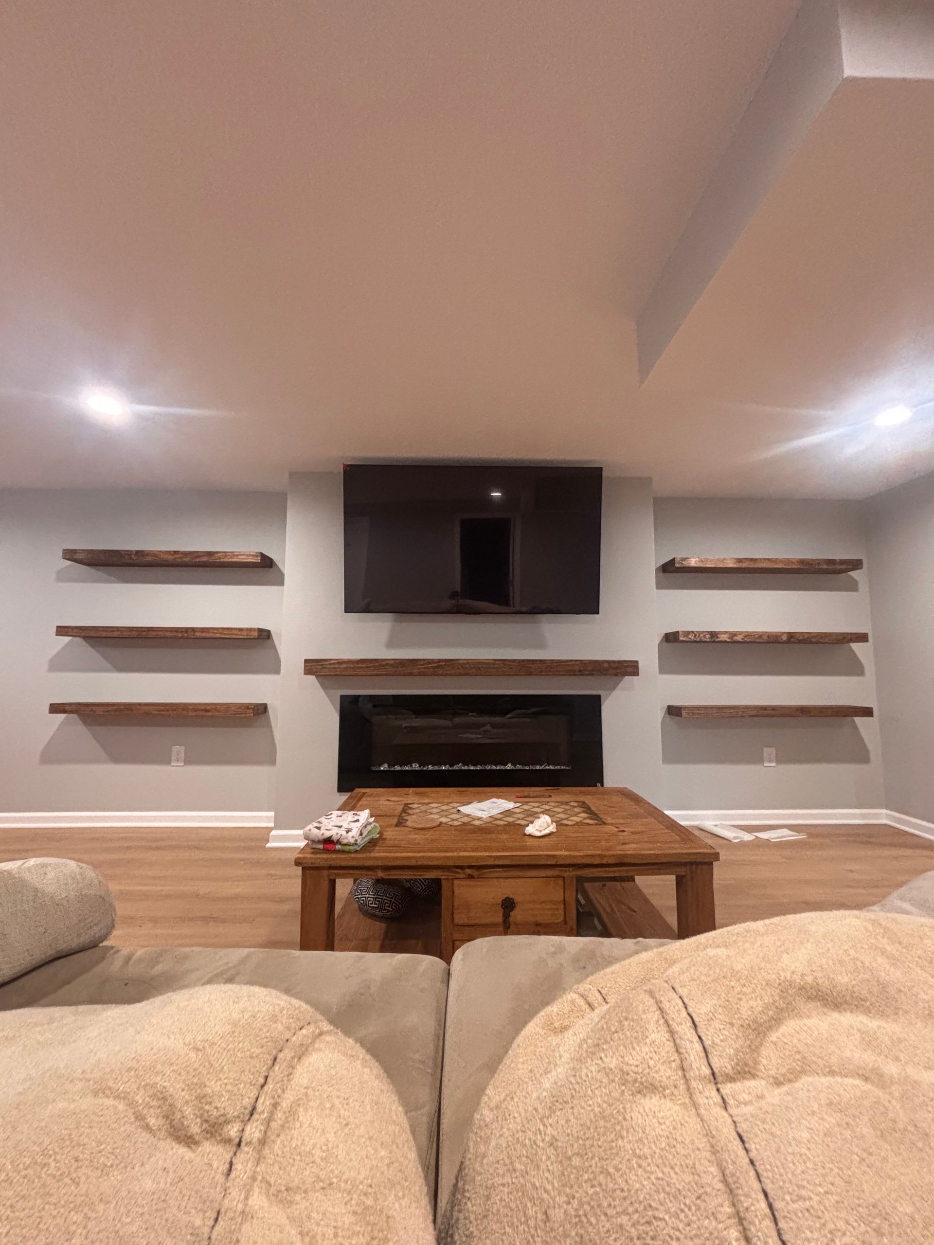 Cozy living room with mounted TV, fireplace, floating shelves, and beige sofas facing a coffee table.