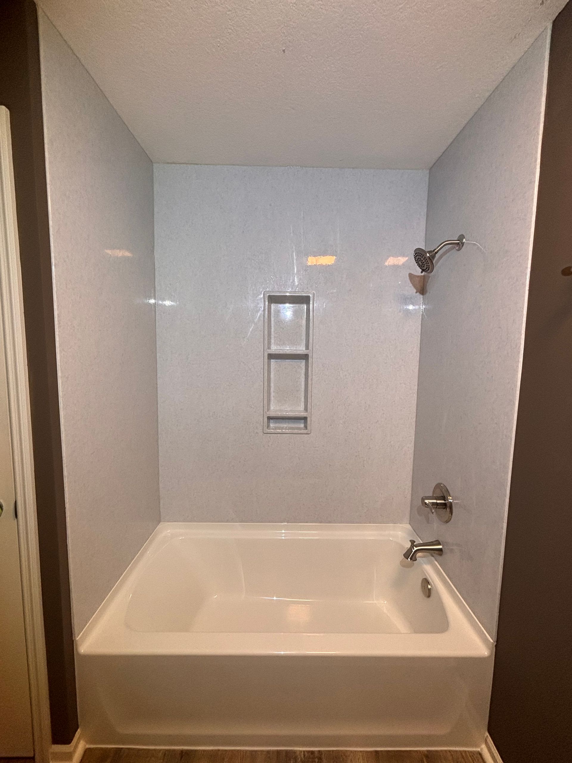 Small white bathtub with shower fixtures in a tiled alcove bathroom.