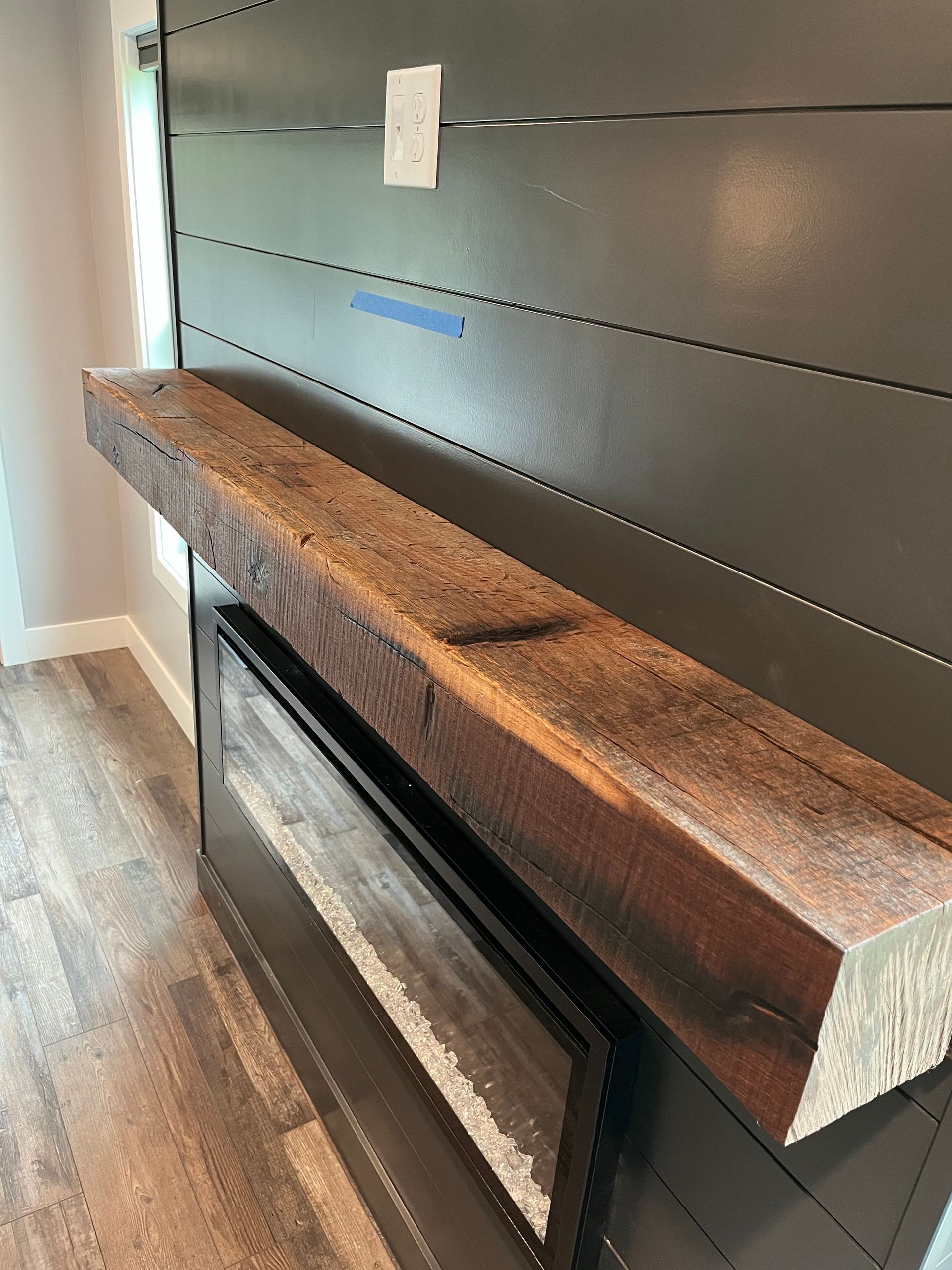 Rustic wood mantel shelf above a modern black electric fireplace on a gray wall
