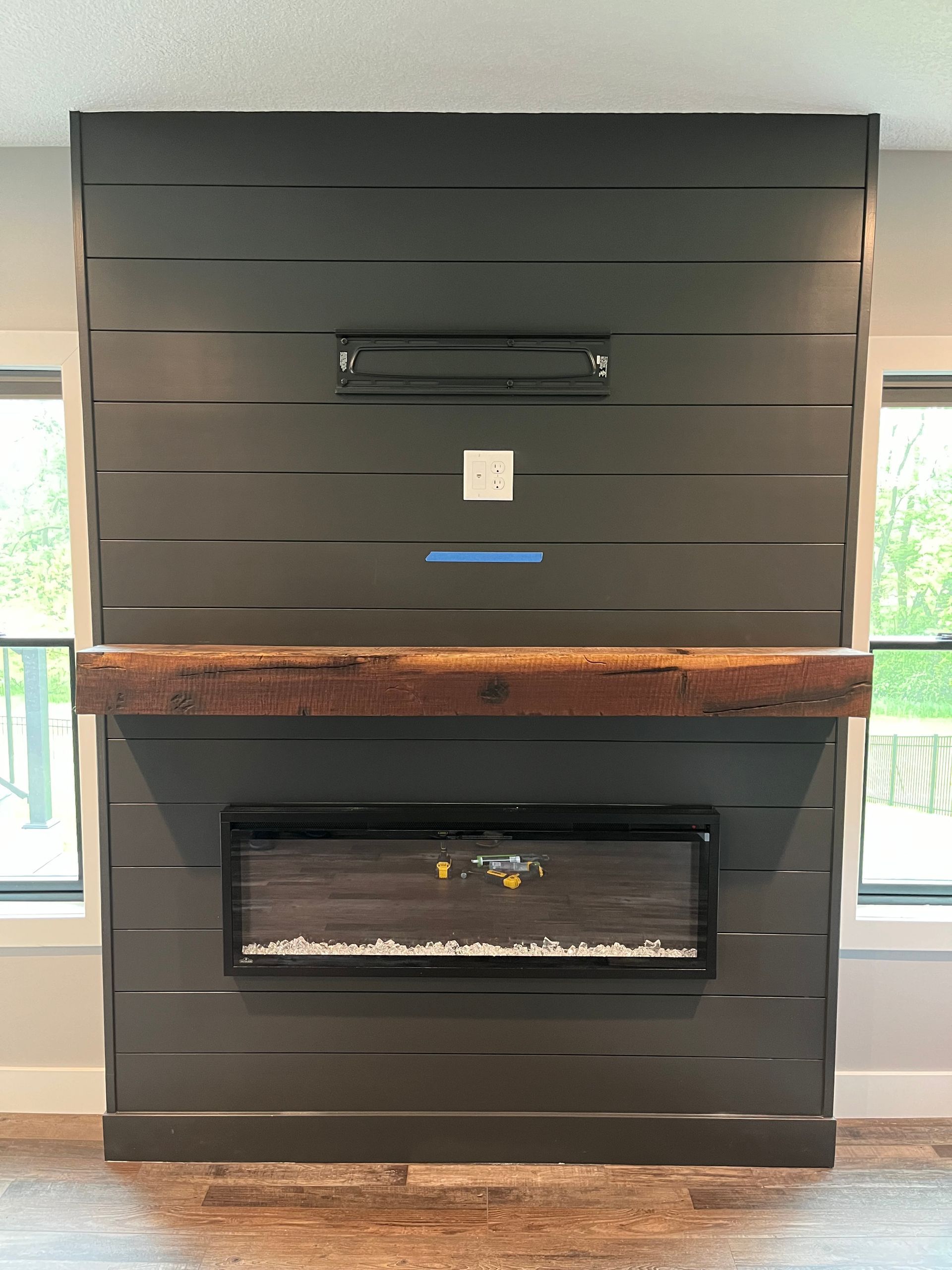 Modern black fireplace wall with a central electric fireplace and a rustic wood mantel shelf.