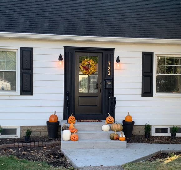 Front porch with Halloween pumpkins flanking a black front door on a white house