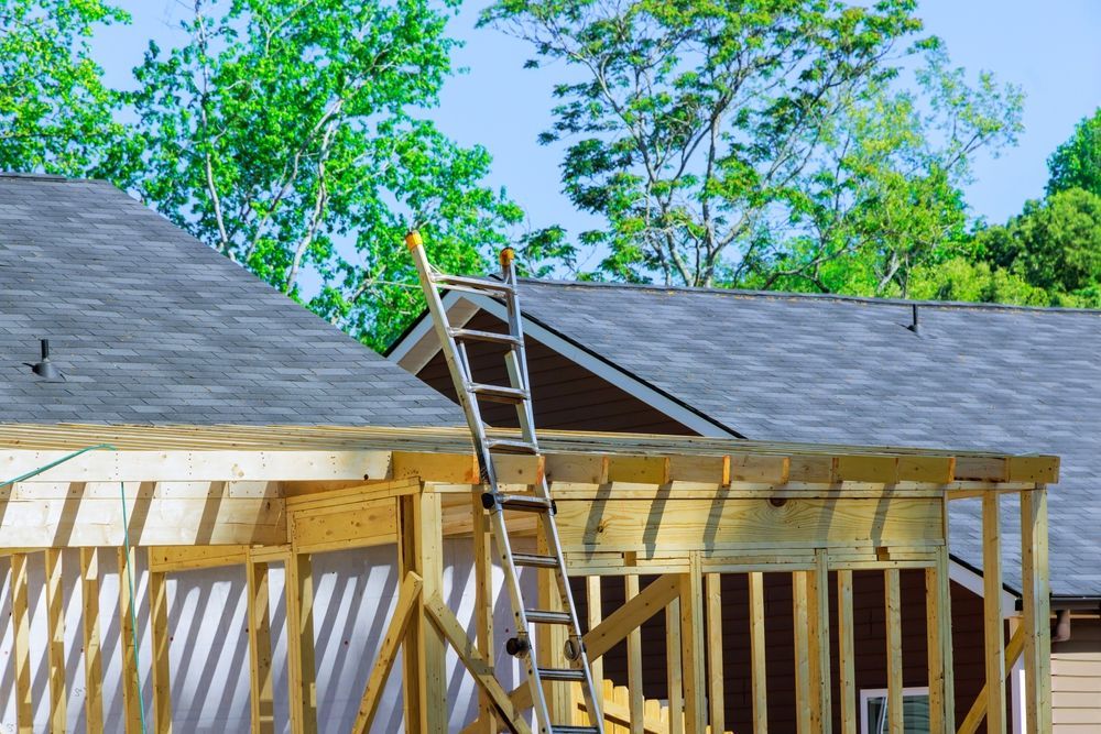 Roofing crew working on a house roof with ladders and exposed framing under a blue sky