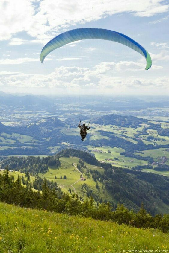 Una persona está haciendo parasailing sobre una ladera cubierta de hierba.