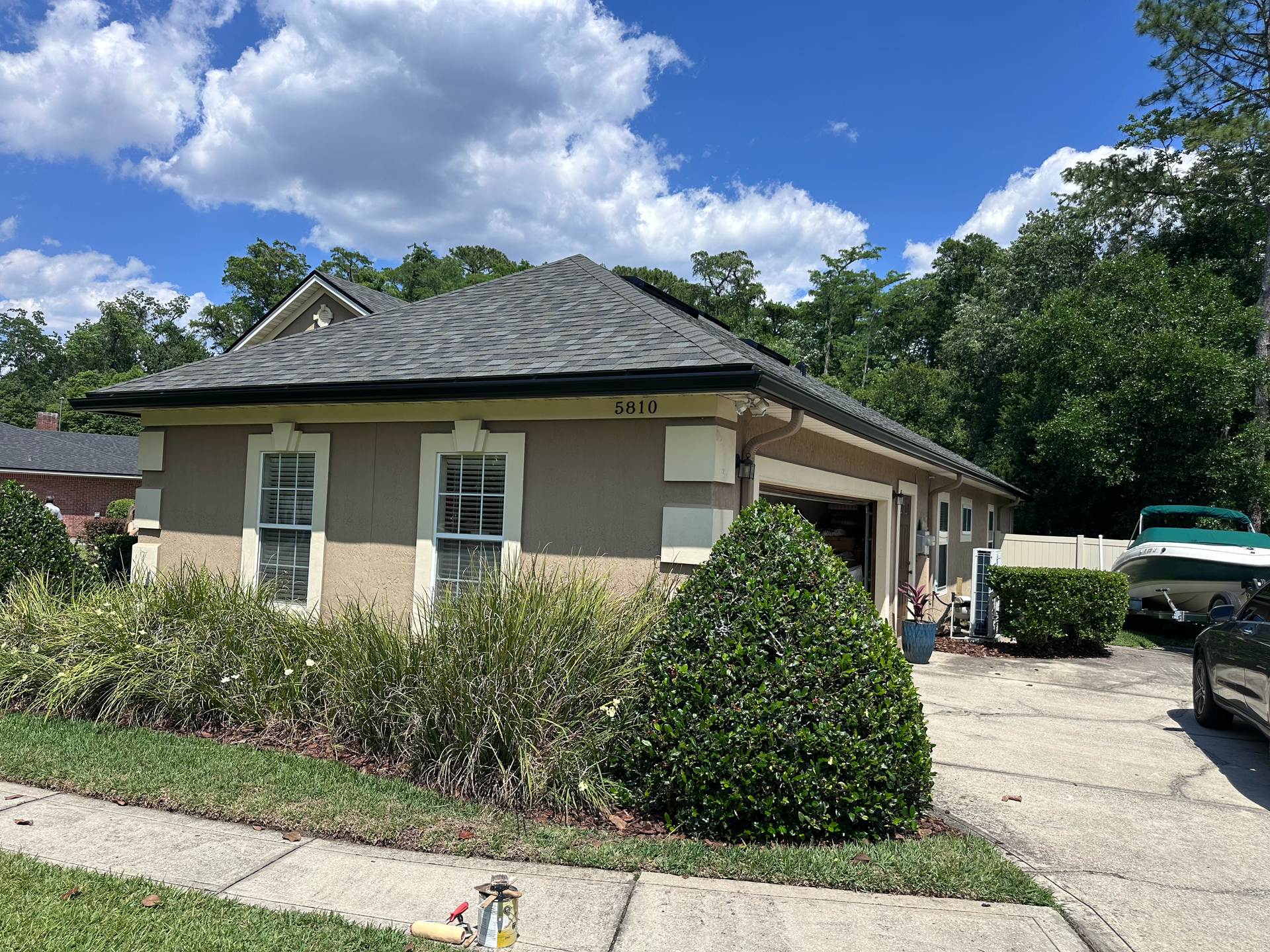 Single-story beige house with a dark roof, front garden, and driveway under a blue sky.