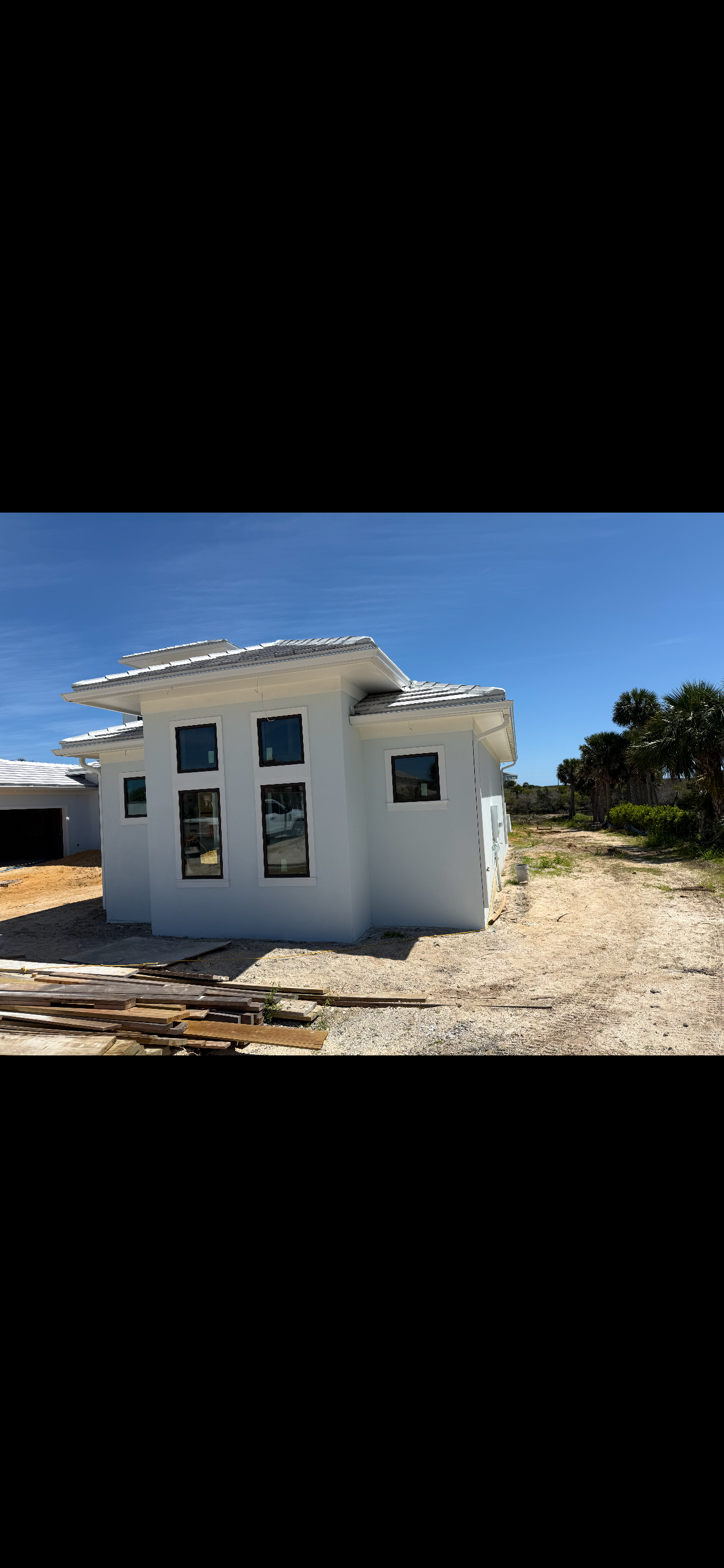 Small white unfinished house under construction on a sunny, sandy lot with blue sky.