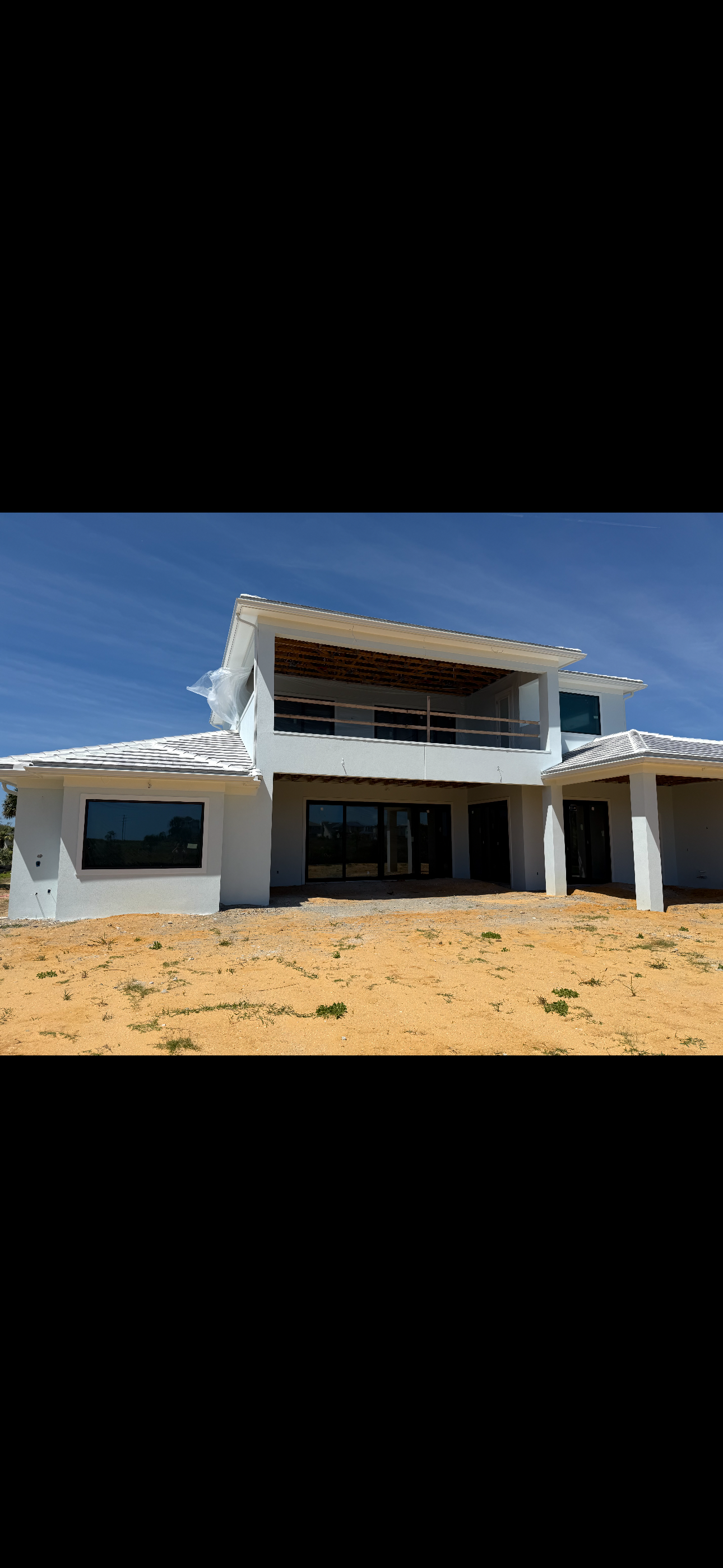 Modern white two-story house under construction on sandy ground beneath a clear blue sky