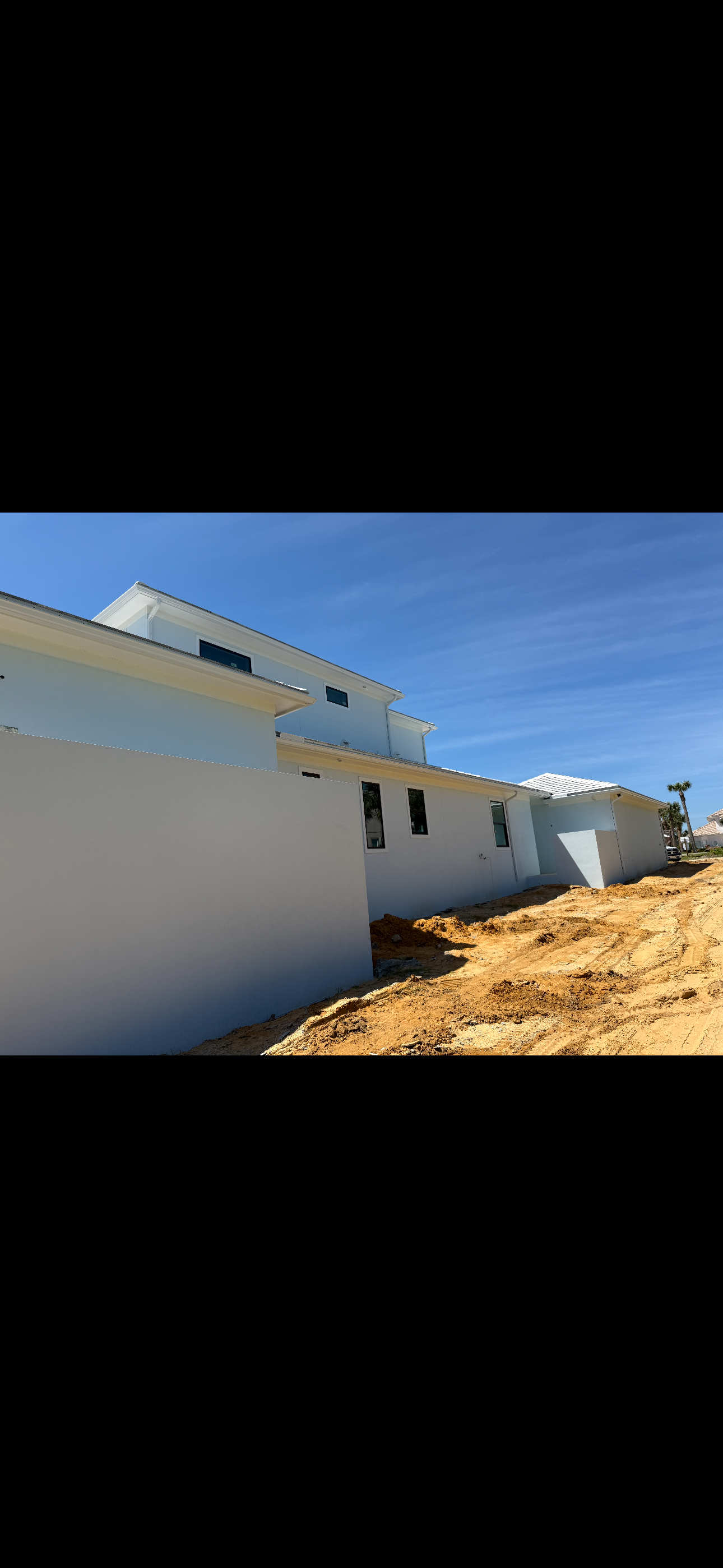 Modern white building exterior with blue accents beside a dirt path under a clear sky