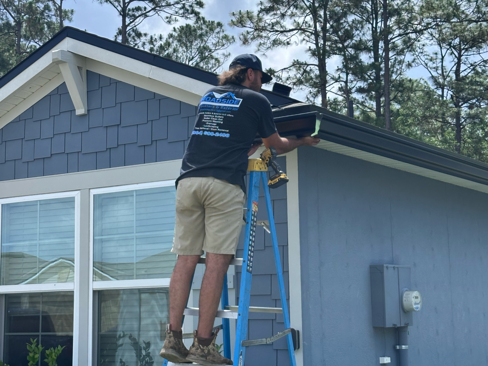 Worker on a ladder repairing the roof edge of a blue house