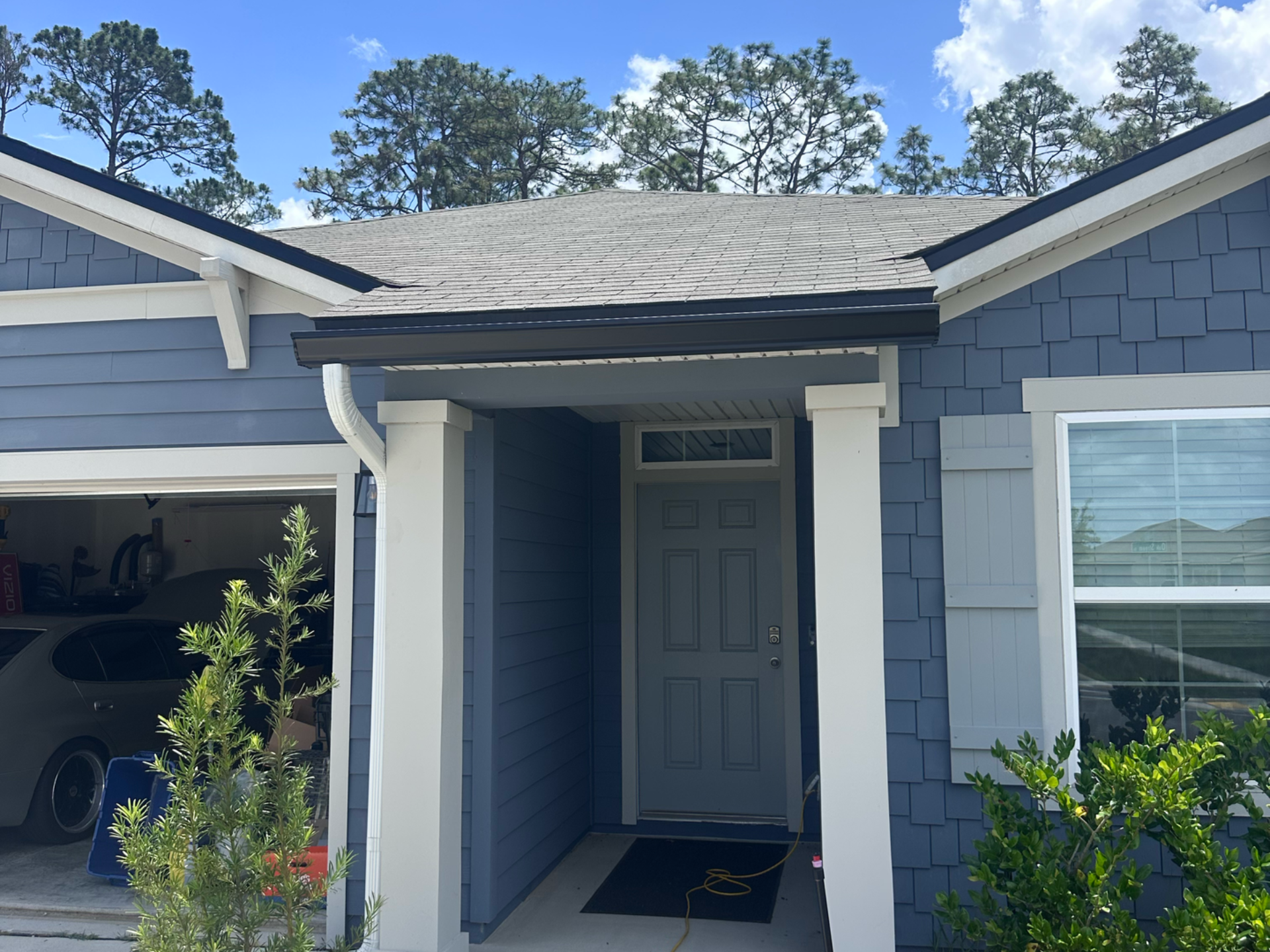 Front entrance of a blue house with a white porch, open garage, and potted plants.