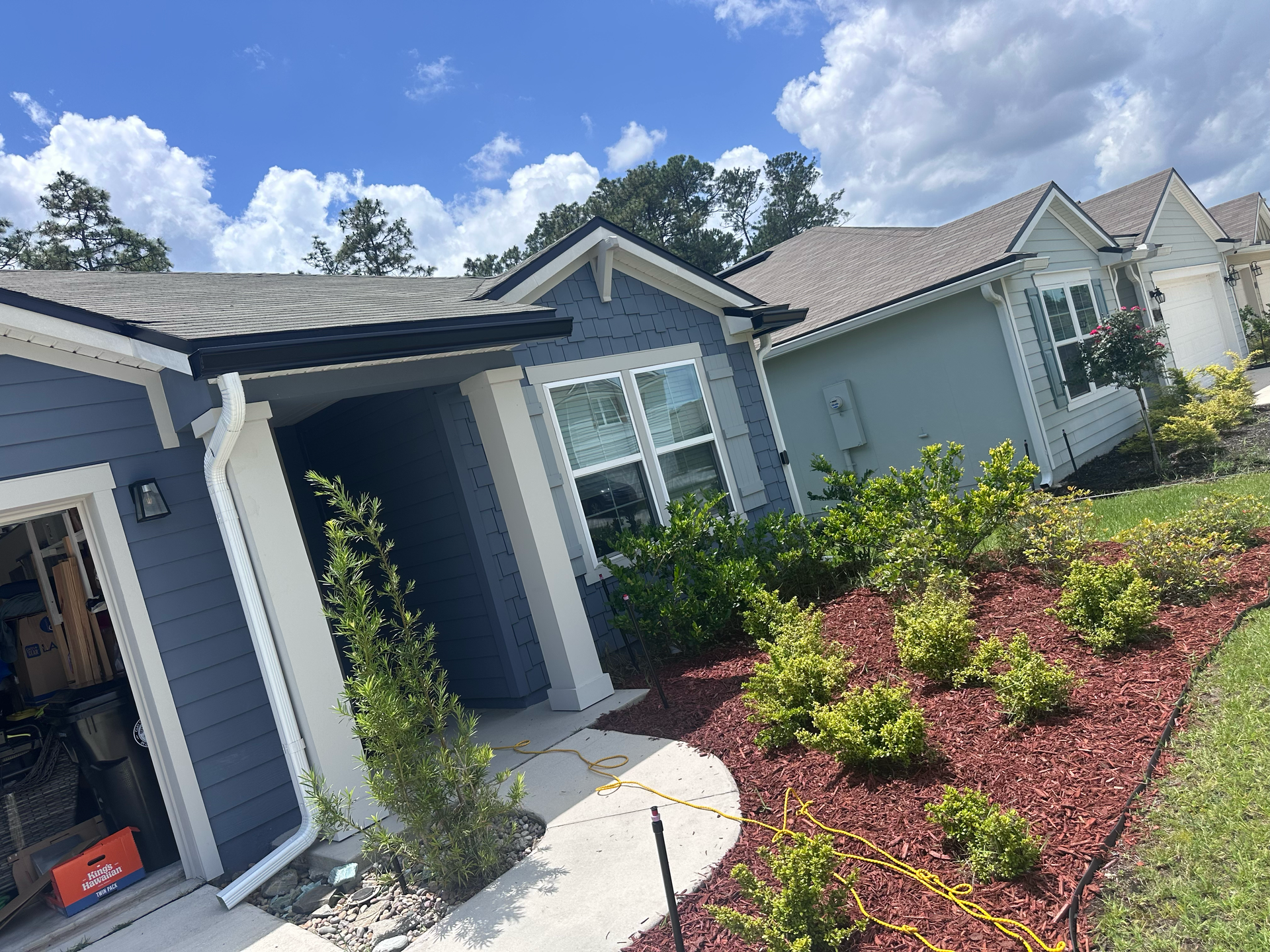 Blue house exterior with white trim, curved walkway, and landscaped red mulch under a cloudy sky