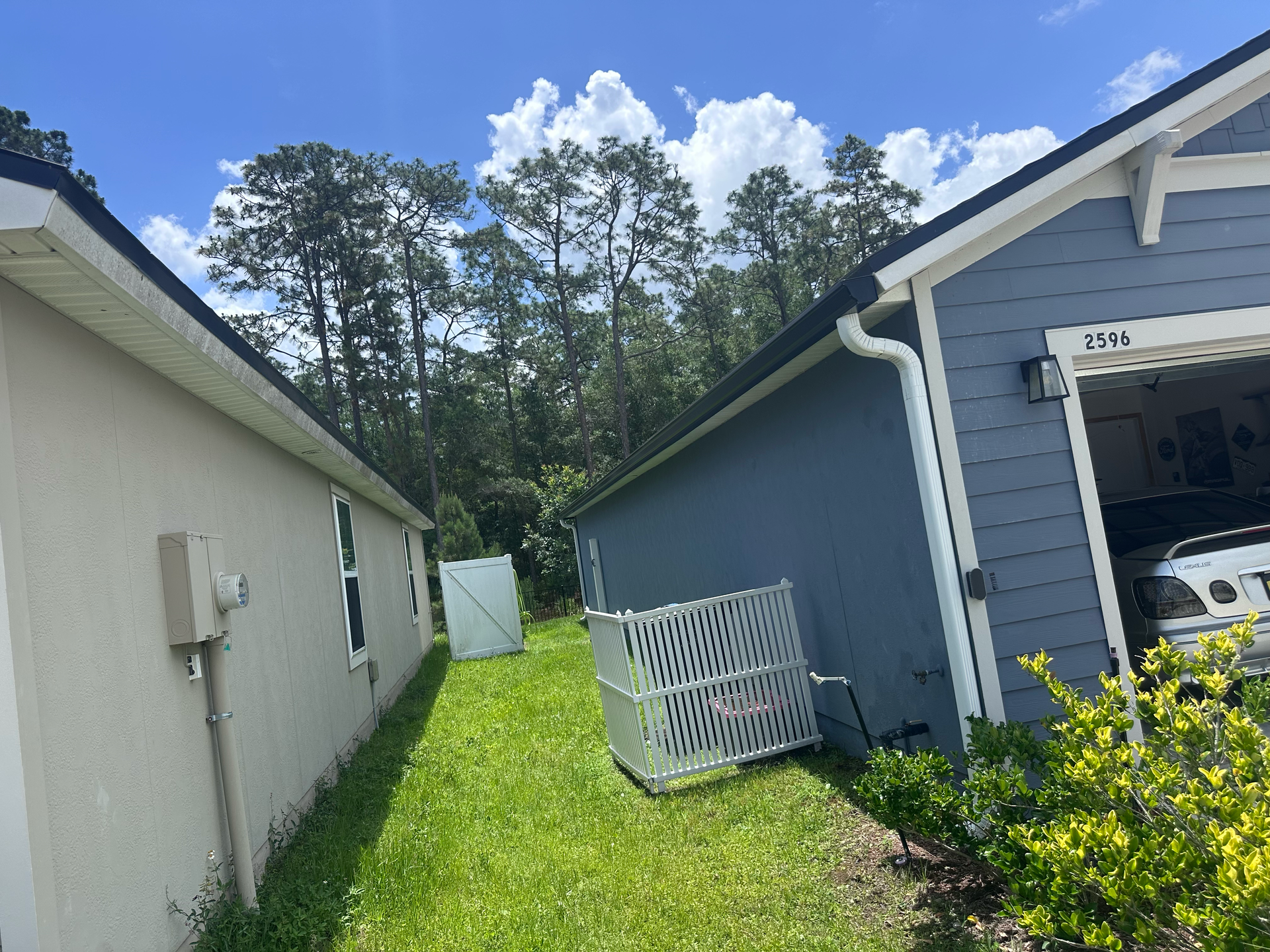 Narrow grassy side yard between two houses, with a white fence panel leaning against the blue house.