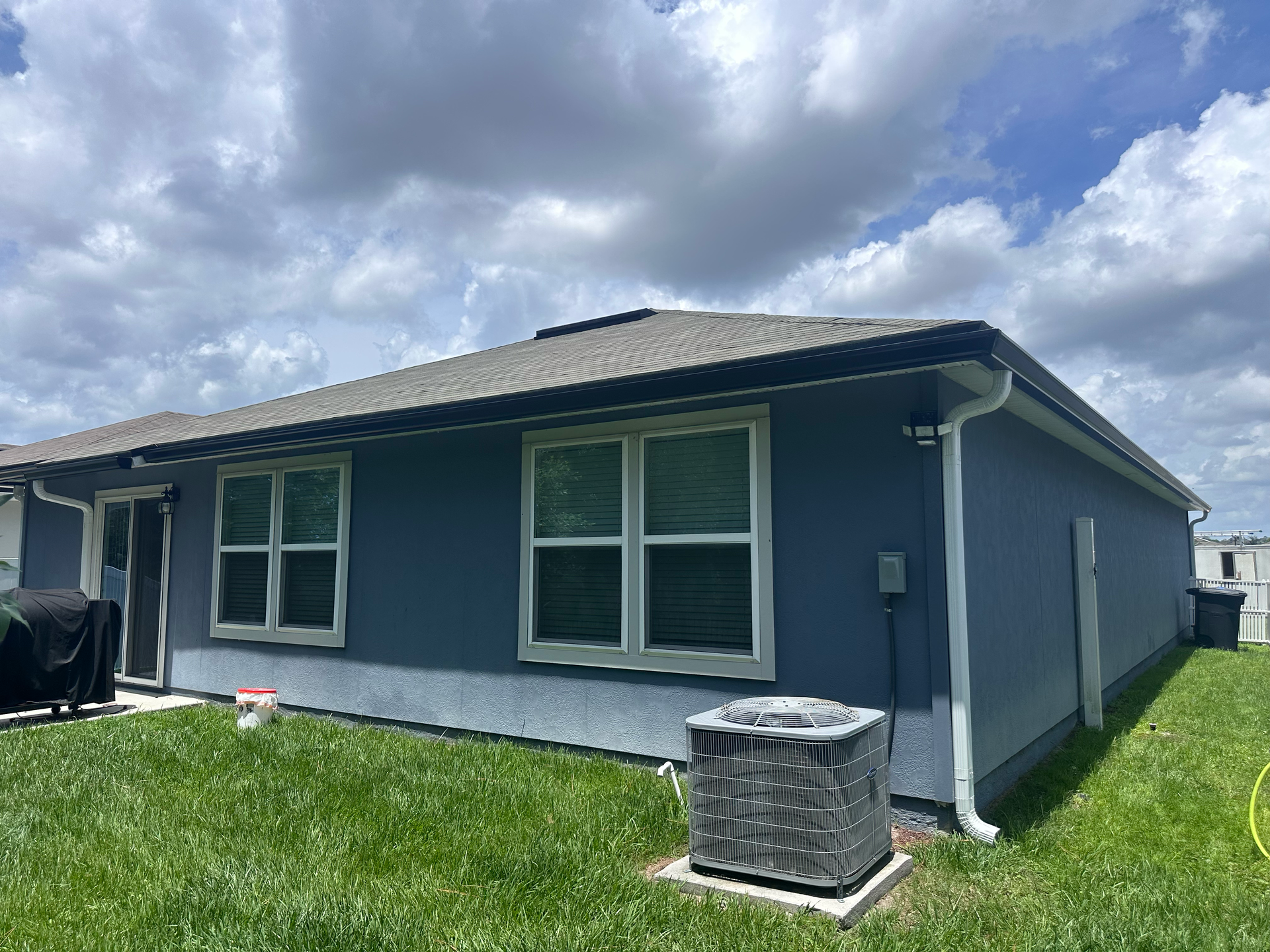 Blue single-story house with white trim and a grassy yard under cloudy skies