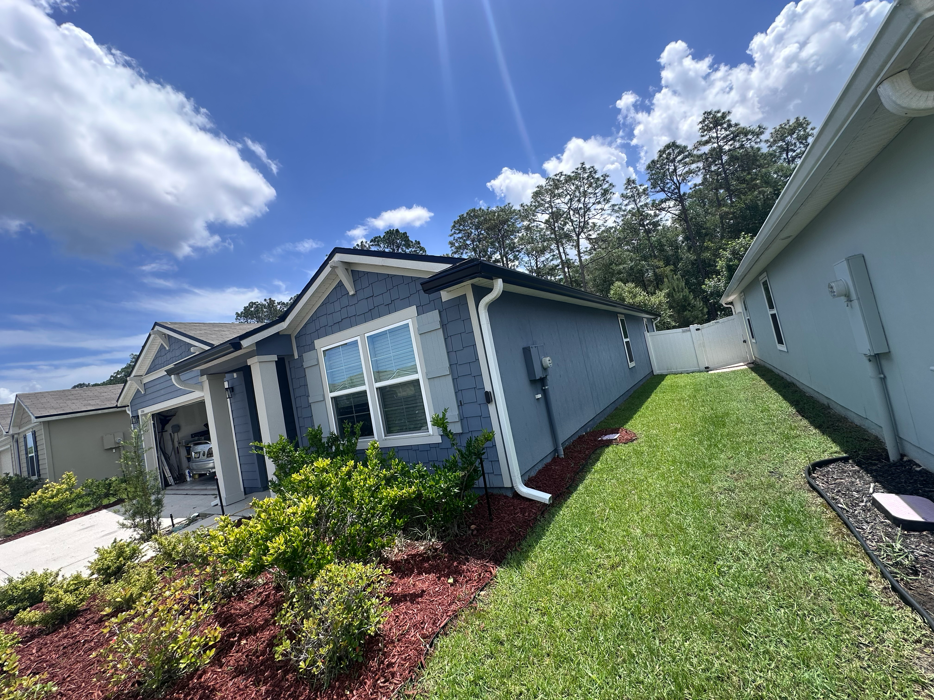 Single-story gray house with white trim, landscaped front yard, and blue sky with clouds